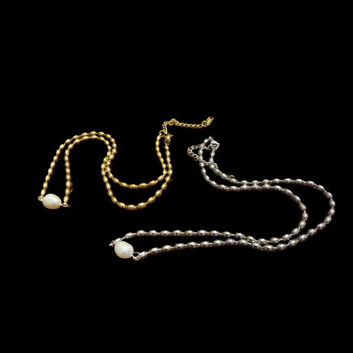 Two necklaces, one gold and one silver, with beaded chains and a unique pearl, on a black background