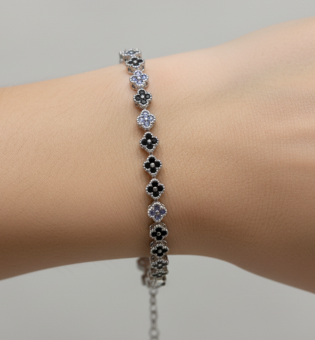 Tennis bracelet with black clover designs on a wrist against a neutral background