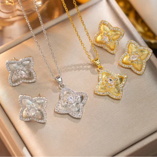 Two matching jewelry sets, each featuring a delicate necklace with a pendant and a pair of stud earrings.  One set is rendered in a gleaming gold  tone, while the other is in a. bright silver tone.