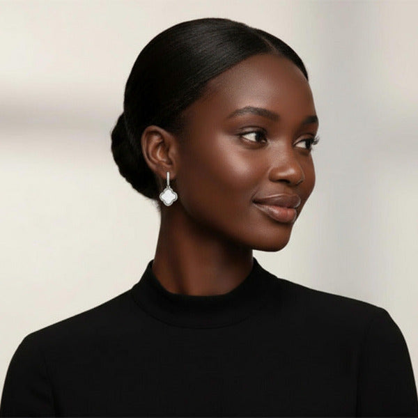 Elegant dangle earrings featuring a classic quatrefoil (four-leaf clover) design in a silver frame. Each earring showcases a small, pave-set huggie hoop, from which a graceful white clover shaped pendant is suspended.