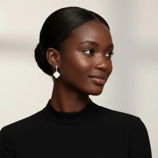 Elegant dangle earrings featuring a classic quatrefoil (four-leaf clover) design in a silver frame. Each earring showcases a small, pave-set huggie hoop, from which a graceful white clover shaped pendant is suspended.