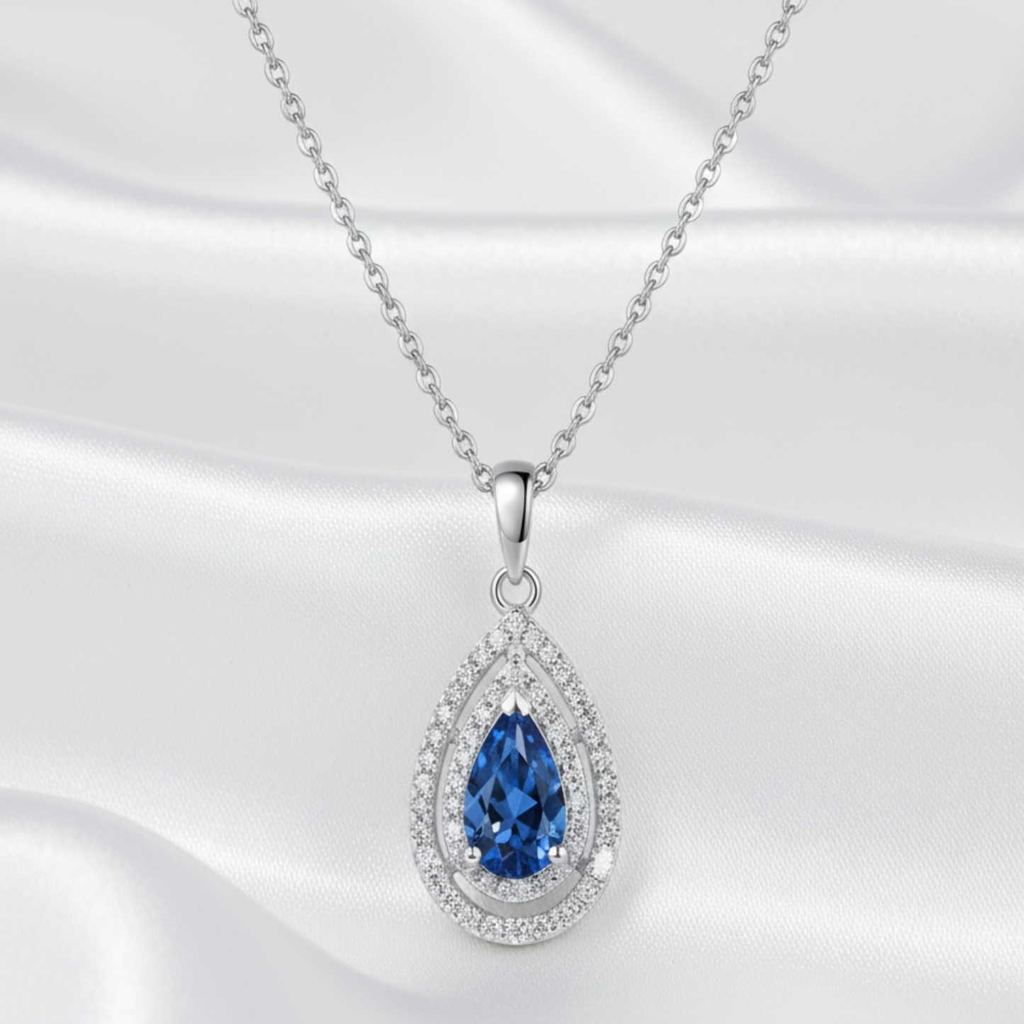 Teardrop-shaped pendant with blue moissanite gemstone and diamond accents on a white background