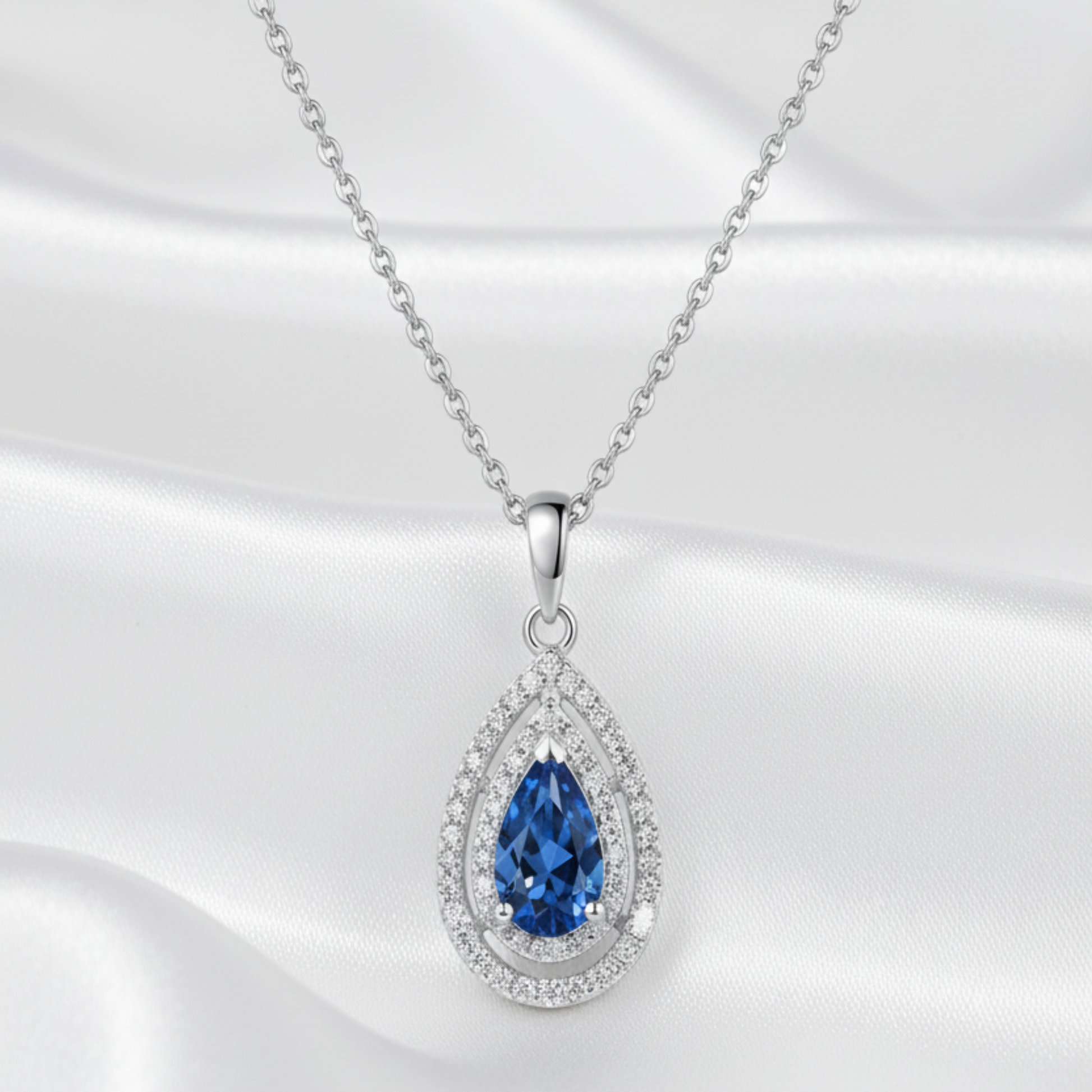 Teardrop-shaped pendant with blue moissanite gemstone and diamond accents on a white background