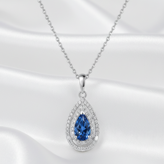Teardrop-shaped pendant with blue moissanite gemstone and diamond accents on a white background