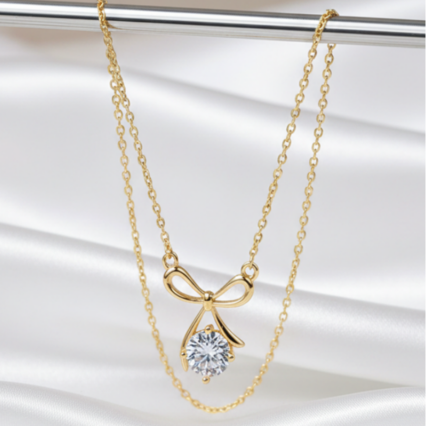 Gold bow-shaped necklace with a clear gemstone pendant on a white background