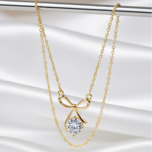 Gold bow-shaped necklace with a clear gemstone pendant on a white background