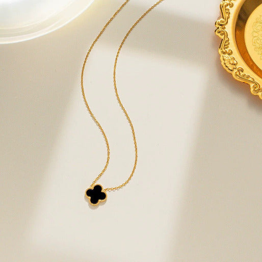 Gold necklace with a clover-shaped pendant on a light beige background