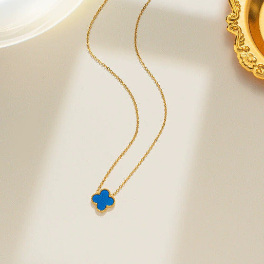 Gold necklace with a blue clover pendant on a light beige background