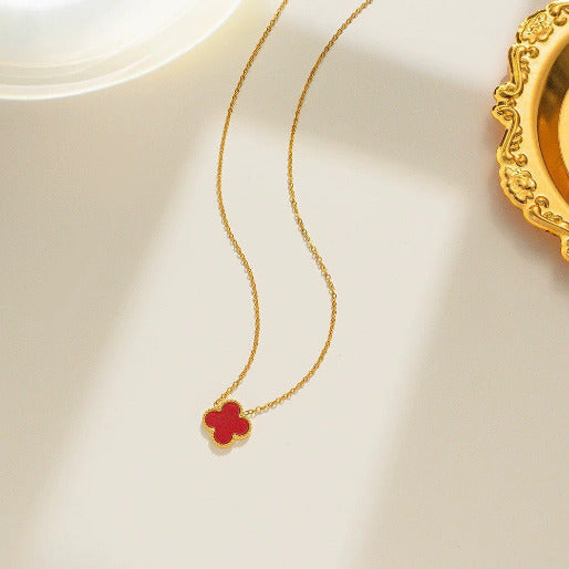 Gold necklace with a red clover pendant on a beige background