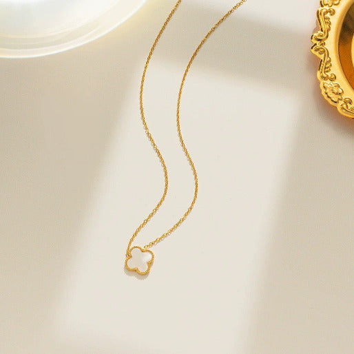 Gold necklace with a clover-shaped pendant on a light beige background