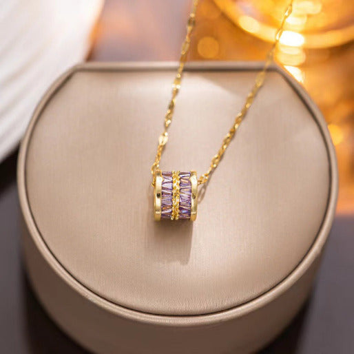 Gold necklace with a purple gemstone pendant on a beige cushion