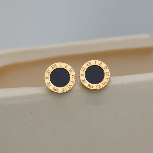 Gold earrings with black centers on a beige surface
