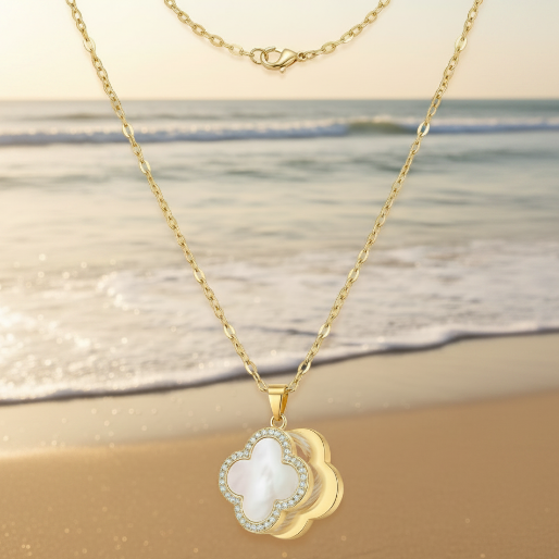 Gold necklace with a clover-shaped spinning pendant on a beach