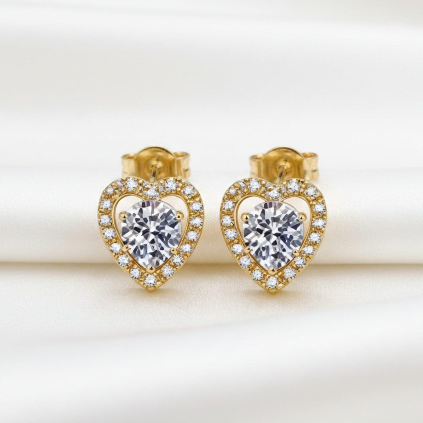 Heart-shaped gold earrings with clear moissanite gemstones on a beige background