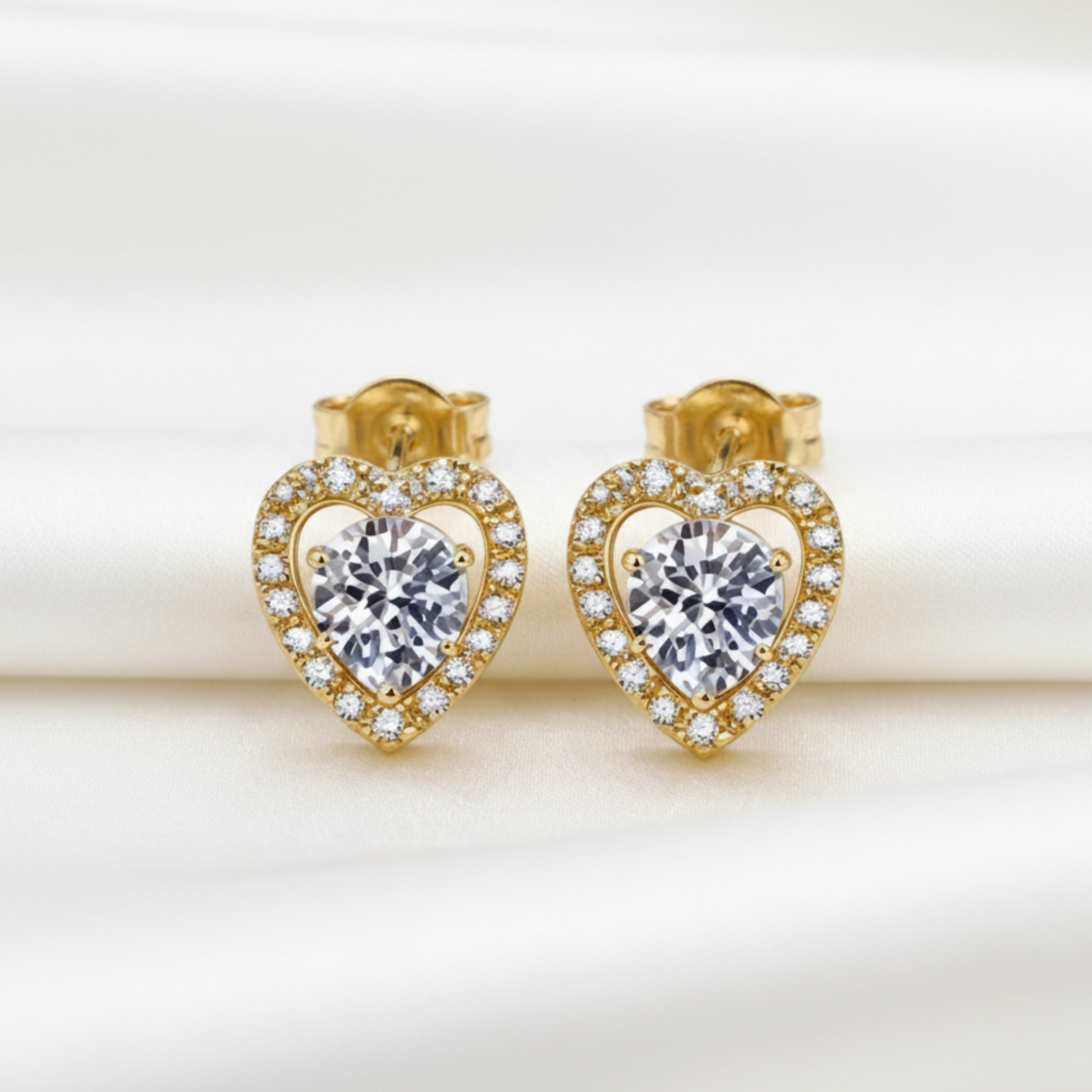 Heart-shaped gold earrings with clear moissanite gemstones on a beige background