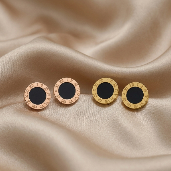 Four round earrings with black centers and gold Roman numeral accents on a beige fabric background.
