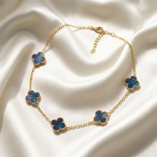 Gold necklace with iridescent blue flower pendants on a white fabric background