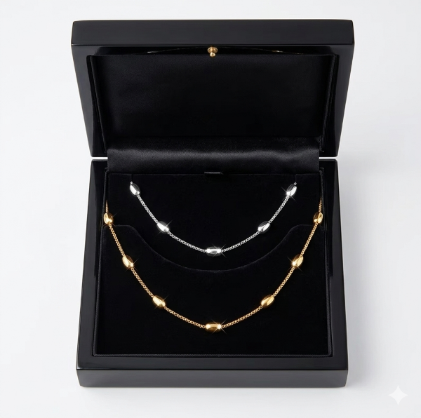 Two necklaces, one gold and one silver, in a black jewelry box on a white background.
