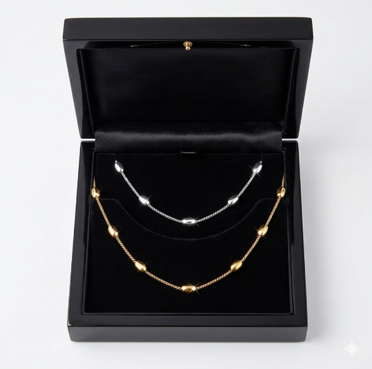Two necklaces, one gold and one silver, in a black jewelry box on a white background.