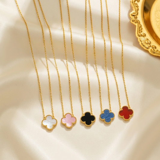 Five gold necklaces with colorful clover pendants on a beige surface.