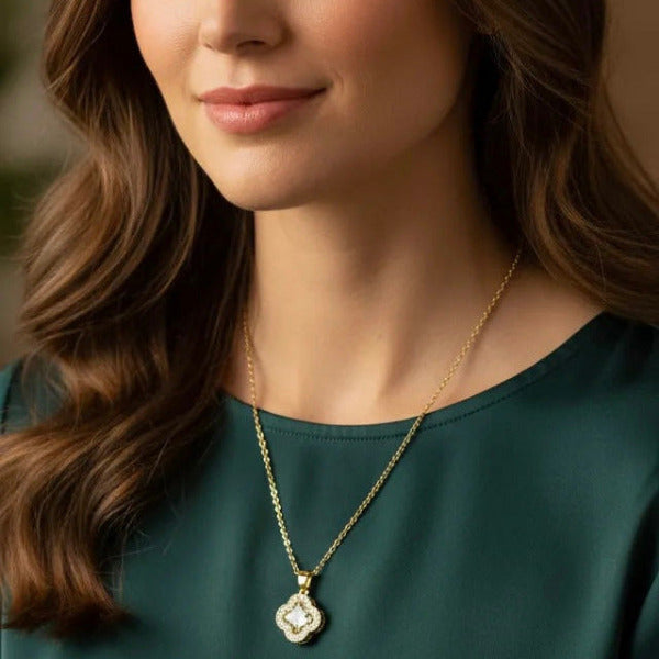 Woman wearing a gold necklace with a clover pendant featuring a central stone, and multiple sparkling accent stones around it.