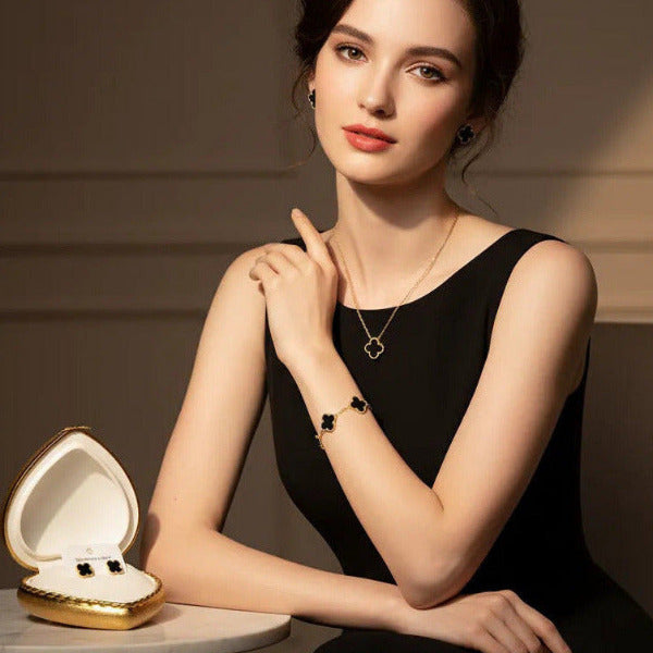 Elegant and gorgeous jewelry set showing a gold necklace with a solitary black clover pendant, a gold bracelet with multiple black clovers, and a pair of black clover stud earrings. All pieces worn together ensures a polished appearance.