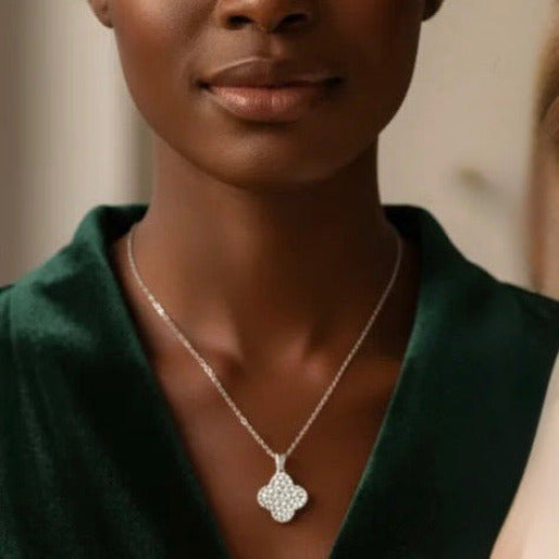 Woman wearing a silver necklace with a white clover pendant with multiple sparkling accent stones in it.