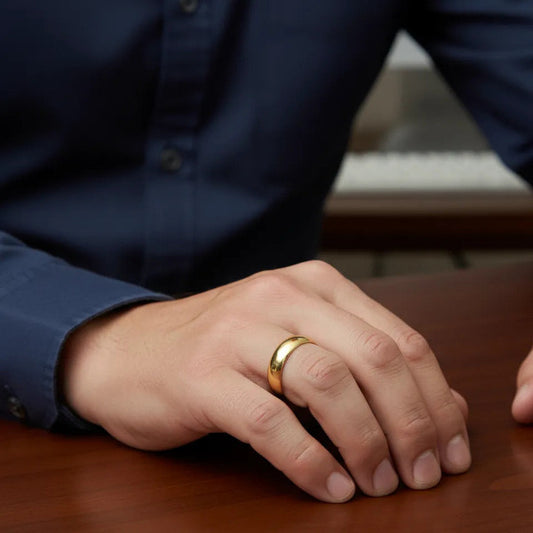 Classic gold tone band ring worn on a finger. It features a simple, smooth, and highly polished surface with a gently domed profile, reflecting light brightly.
