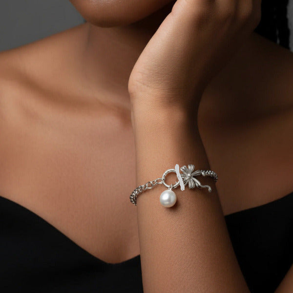 Elegant platinum plated charm bracelet featuring a role-style chain and a secure toggle clasp. Two charms are prominent depicting a delicate bow and a faux pearl, and adorn the bracelet. Designed to be worn on the wrist, this type of bracelet is a classic accessory.