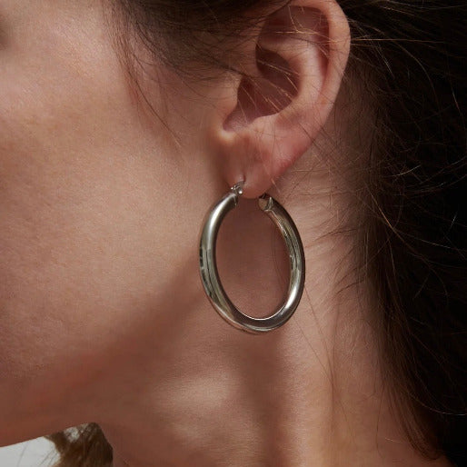Silver hoop earring worn by a person. These versatile earrings are a timeless accessory, suitable for various occasions, from everyday wear to more formal events.