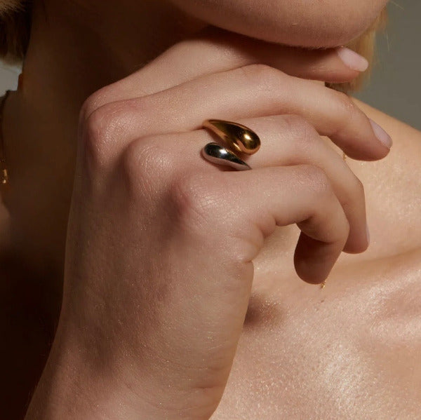 This is a hand wearing a stylish bicolor twist ring featuring a contemporary, open ended design. It combines two distinct metallic finishes, gold and silver, in an elegant overlapping or 'twist' formation.