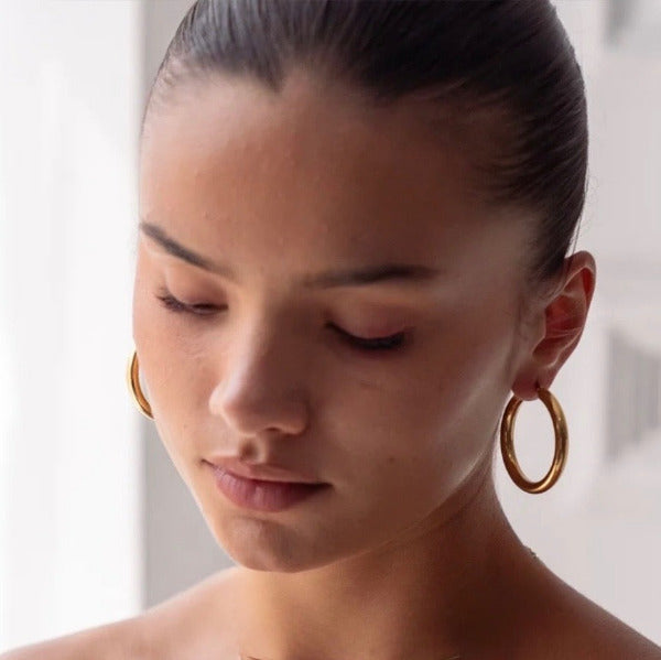 Close-up of a person wearing gold hoop earrings, characterized for their perfectly circular shape and polished, reflective surface.