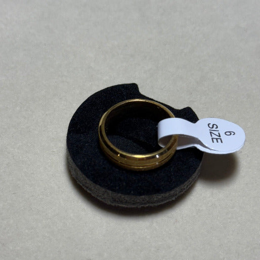 Gold ring on a black cushion with a size tag '6'. 