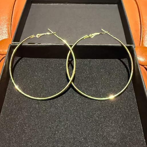 These are a pair of large circular hoop earring, gold in color, made of stainless steel and plated with 18K gold. They feature a french lock clasp, designed for secure wear. With a diameter of 50mm, these earrings are designed to make a noticeable statement.