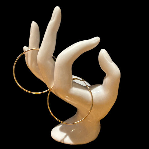 Gold hoop earrings on a white mannequin hand against a black background