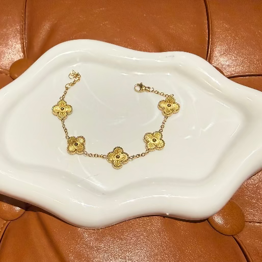 Gold bracelet with clover designs on a white dish against a brown leather background