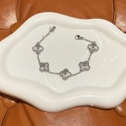 Silver bracelet with multiple clover motif on a white ceramic dish with a brown leather background