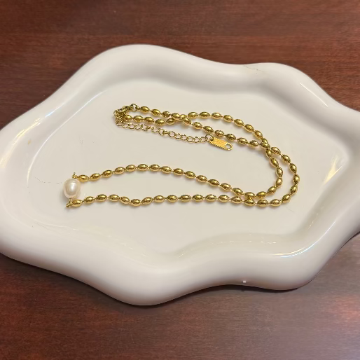 Gold necklace with a pearl on a white dish on a wooden surface