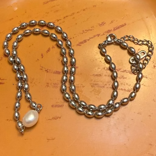 Silver necklace with a pearl pendant on an orange surface