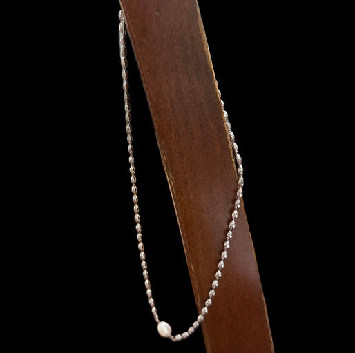Silver beaded necklace hanging on a wooded stick, with a gorgeous pearl as unique pendant.