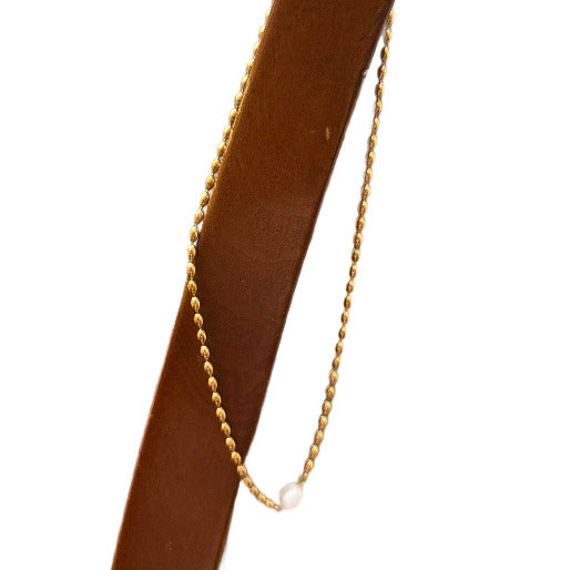 Gold beaded necklace hanging on a wooded stick, with a gorgeous pearl as unique pendant.