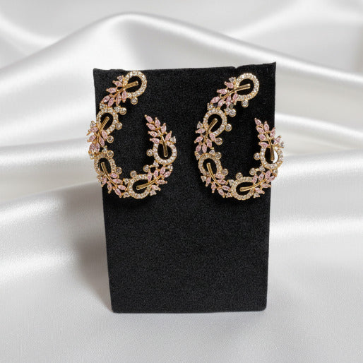 Pair of gold and pink earrings on a black stand.