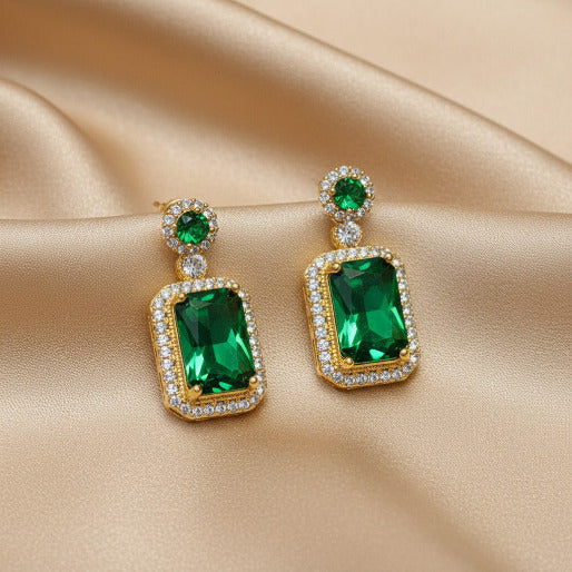 Pair of emerald green earrings with gold accents on a beige background