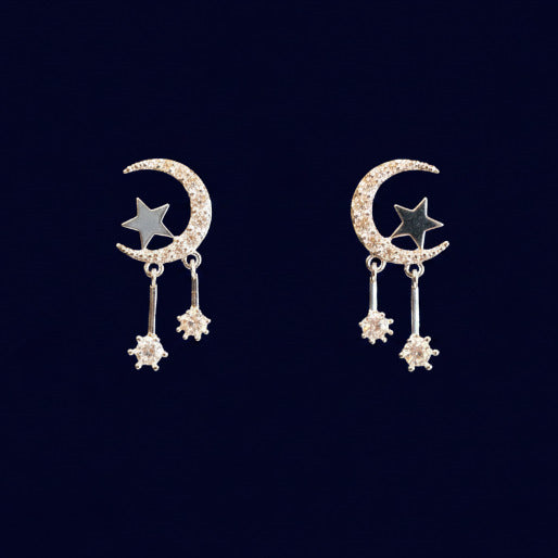 Silver pair of earrings with moon and star designs on a black background