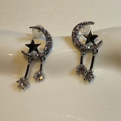 Pair of silver moon and star earrings on a white surface