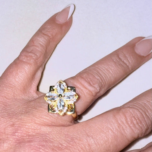 Gold ring with a clear gemstones creating a clover flower, on a finger.