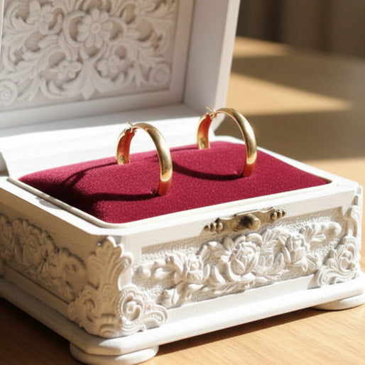 Decorative jewelry box with gold hoop earrings on a red cushion