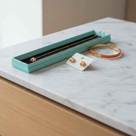 This is the complete jewelry set, highlighting the consistent design language across the bracelet, earrings, and necklace. The uniform application of the rich orange enamel against the 18K gold plated metal, creates a cohesive and luxurious look.