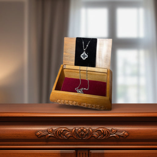Wooden jewelry box with a silver necklace with a black clover pendant.