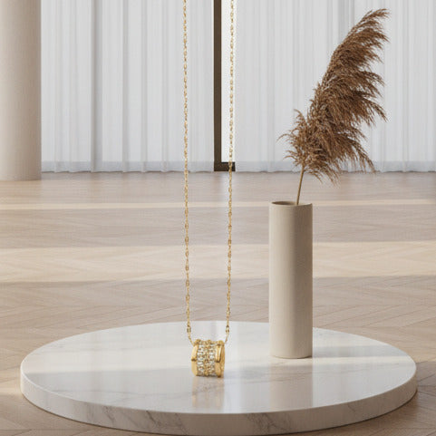 This elegant gold plated necklace features a distinct cylindrical pendant with cubic zirconia.